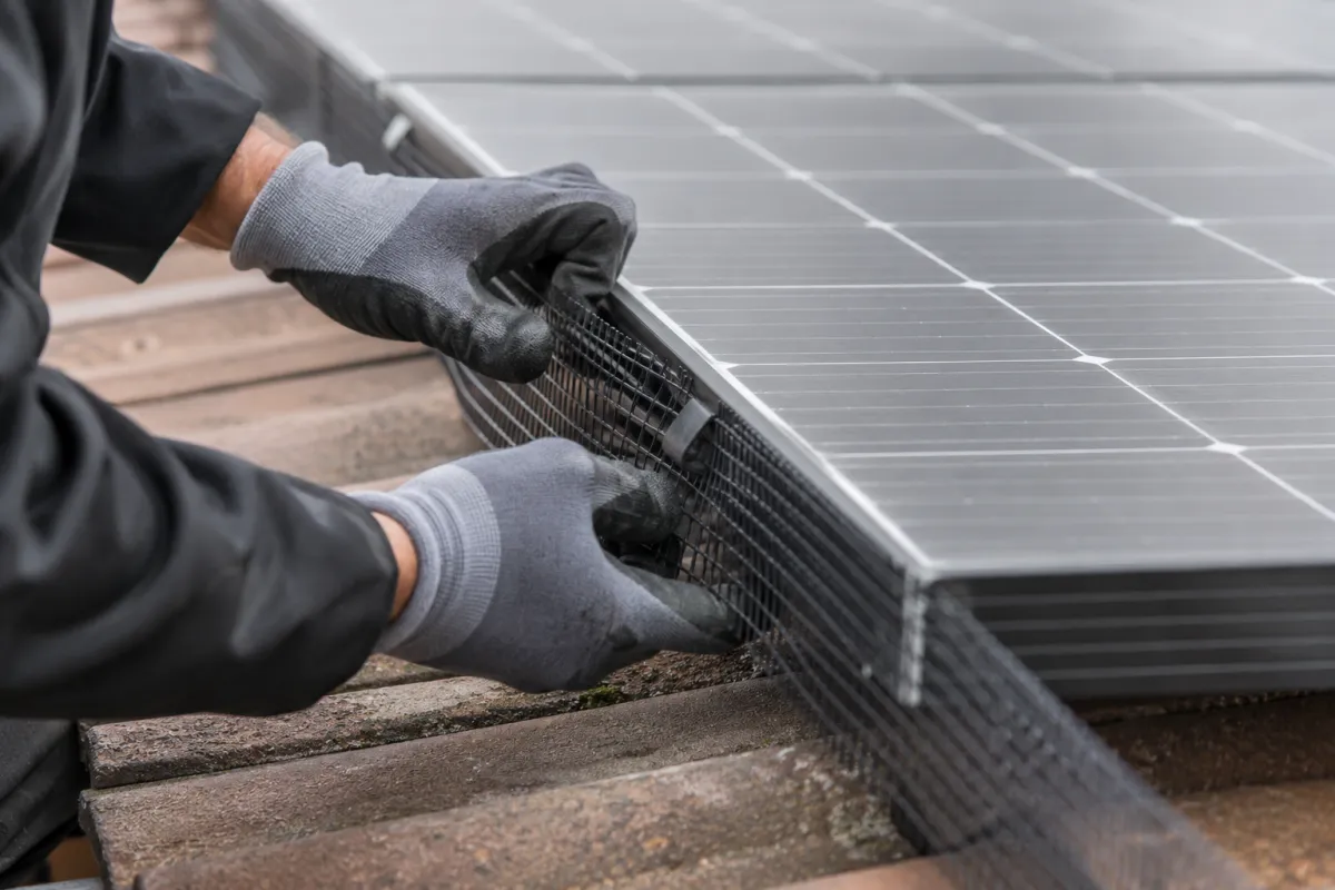 Gloved hands fitting a mesh guard around the edge of rooftop solar panels